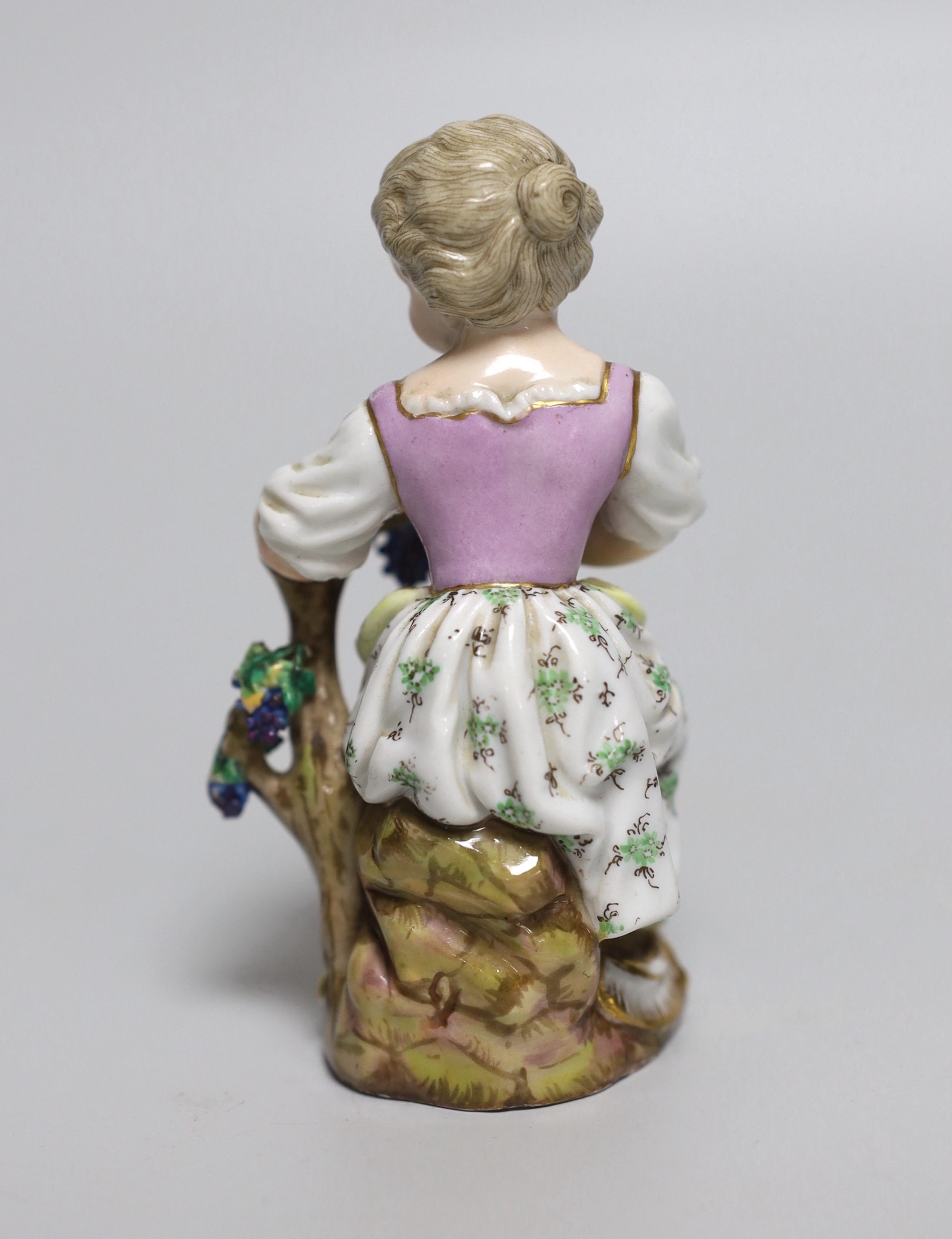 An early 19th century Meissen figure of a girl seated on a tree stump holding a bunch of grapes, painted 58, incised mark and feint crossed swords in blue, 11cm